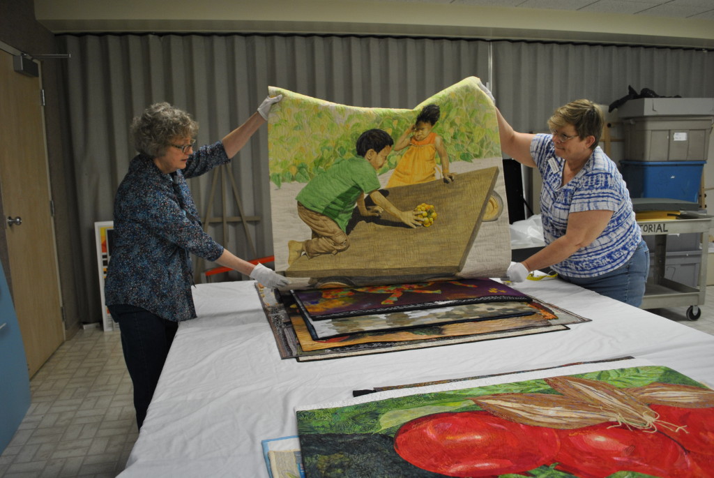 Volunteers from the Shawnee Quilters unpack the Food for Thought exhibit from SAQA at the National Quilt Museum and create condition reports on each quilt. Source: The National Quilt Museum
